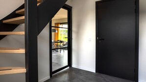A modern interior with a staircase, a dark door, and a view into a dining area.