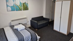 Quarto com cama, sofá cinzento, guarda-roupa e duas pinturas de flores na parede.