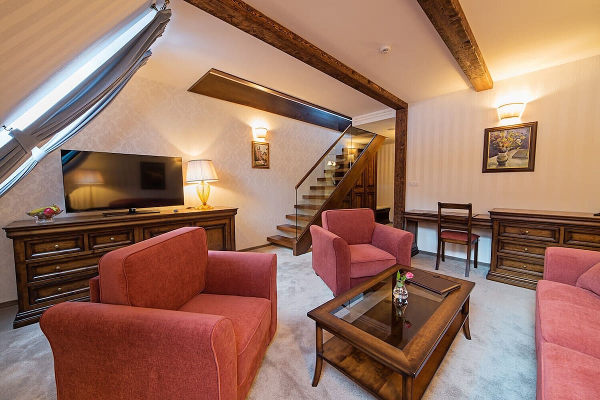 A spacious living room with a large flat-screen TV, two red armchairs, a glass coffee table, and a wooden staircase.