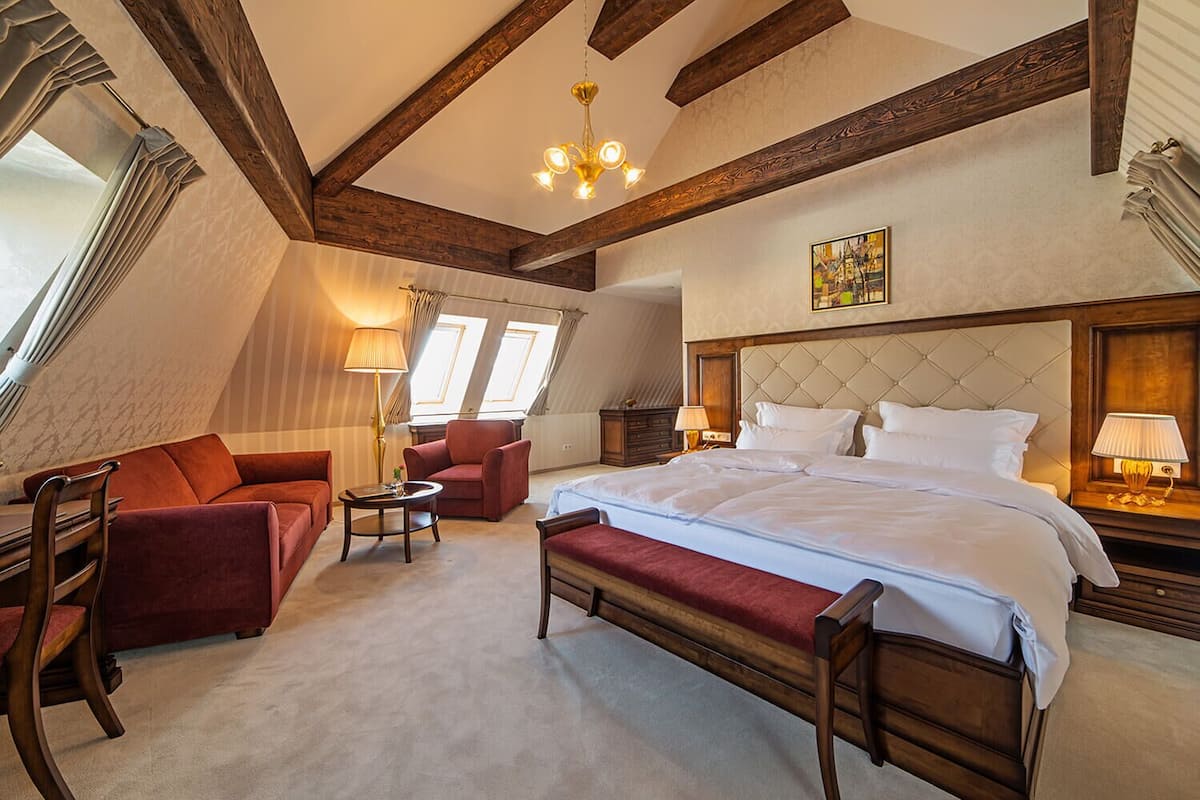A bedroom with a large bed, a red sofa, a small table, and a chandelier.