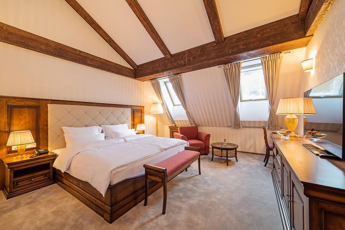 A hotel room with a large bed, a desk with a chair, a small round table, and a television.