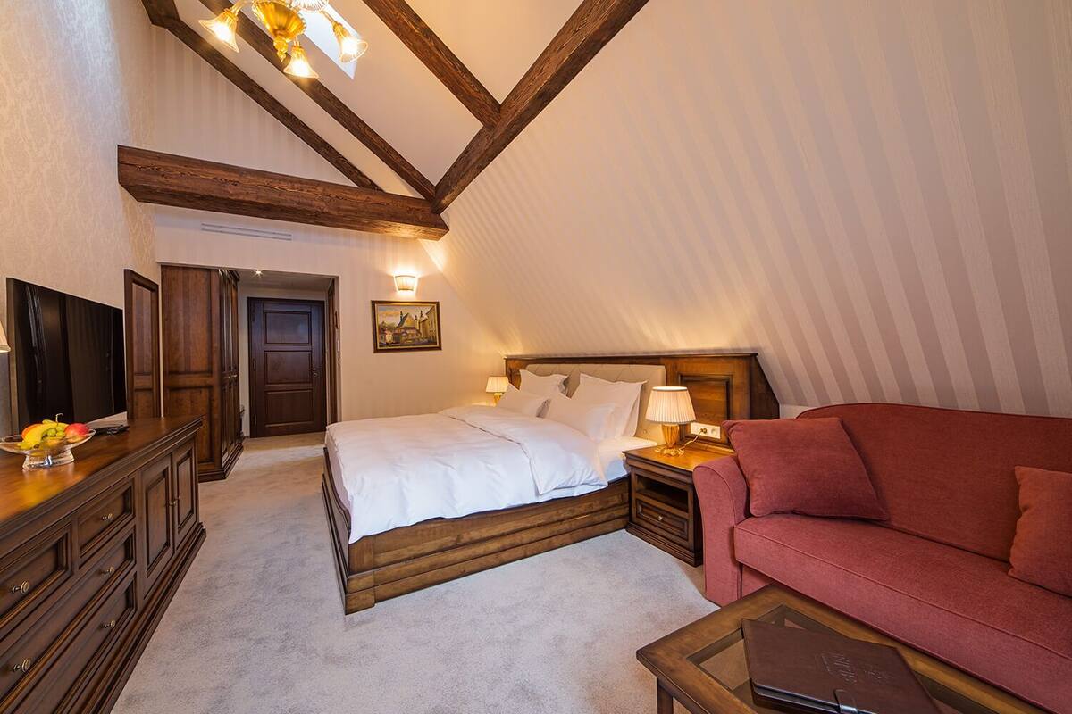 A bedroom with a bed, bedside tables, a red sofa, a wooden dresser, and a painting on the wall.