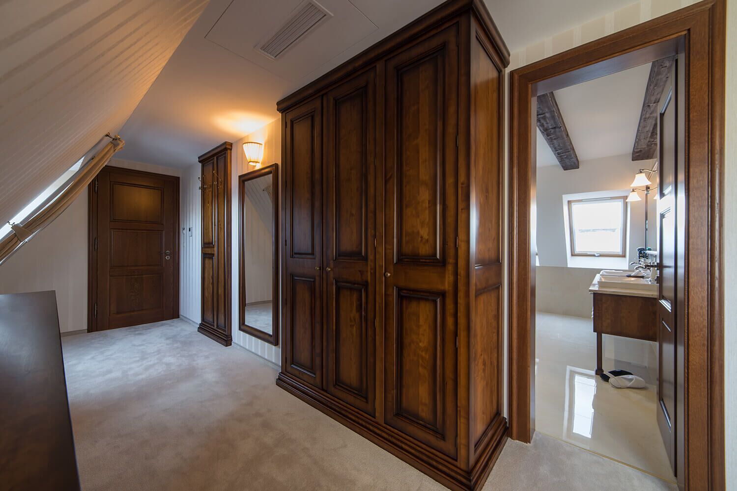 Una habitación con un amplio armario de madera, un espejo y un baño con lavabo y ventana.