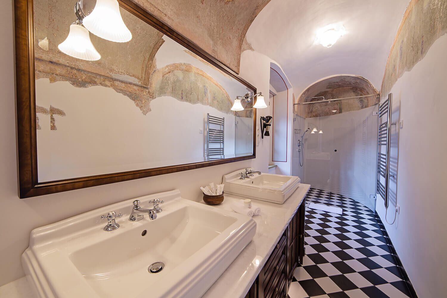Une salle de bain avec deux lavabos, un grand miroir et un sol à carreaux noirs et blancs.