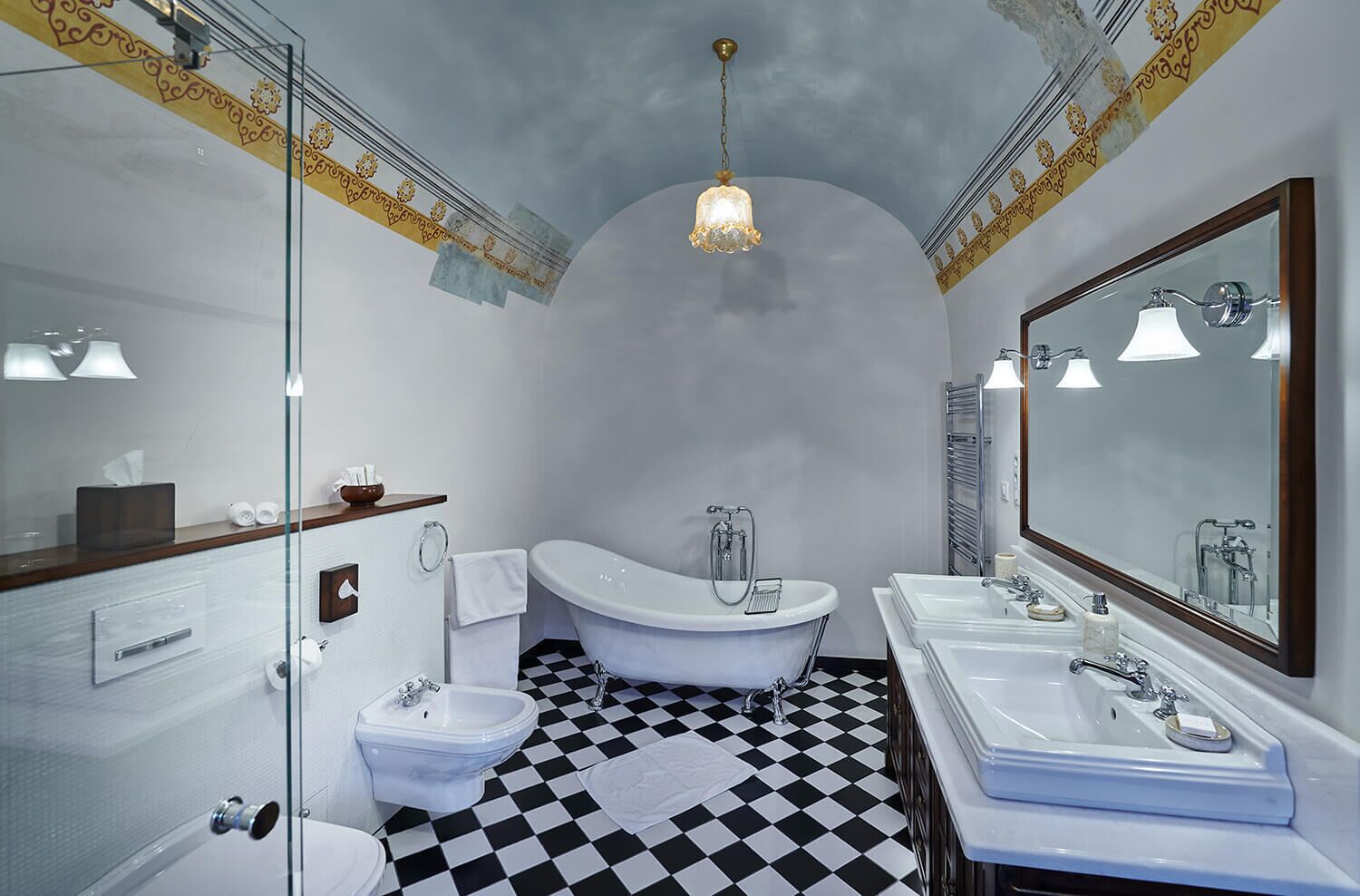 A bathroom with a checkered floor, a freestanding bathtub, two sinks, and a large mirror.