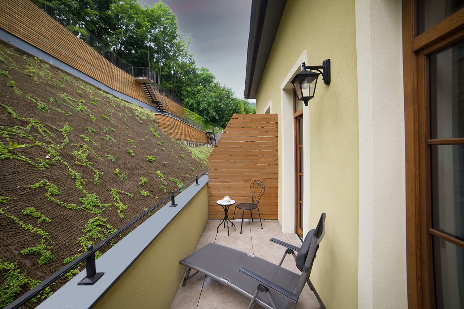 A balcony with a green wall, a wooden staircase, and a table with chairs.