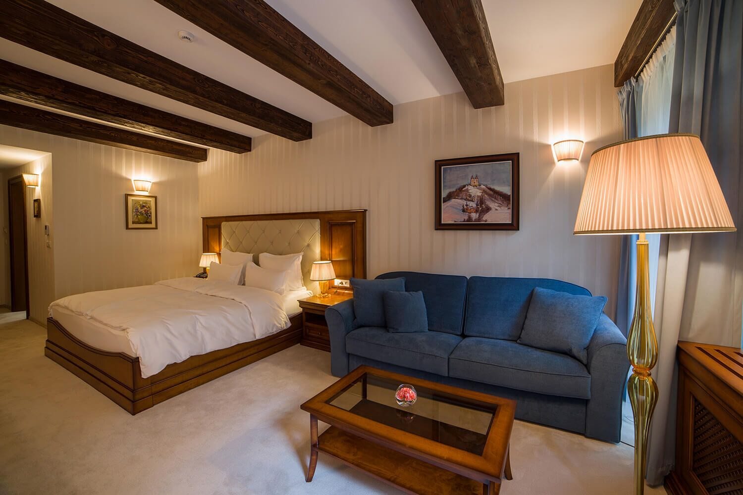 A hotel room with a bed, a sofa, a coffee table, and a lamp.