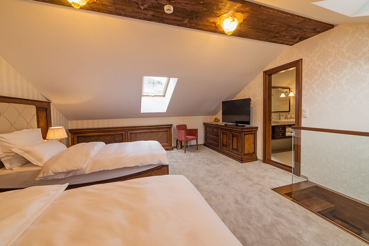 A bedroom with two beds, a TV, a red chair, and a skylight.