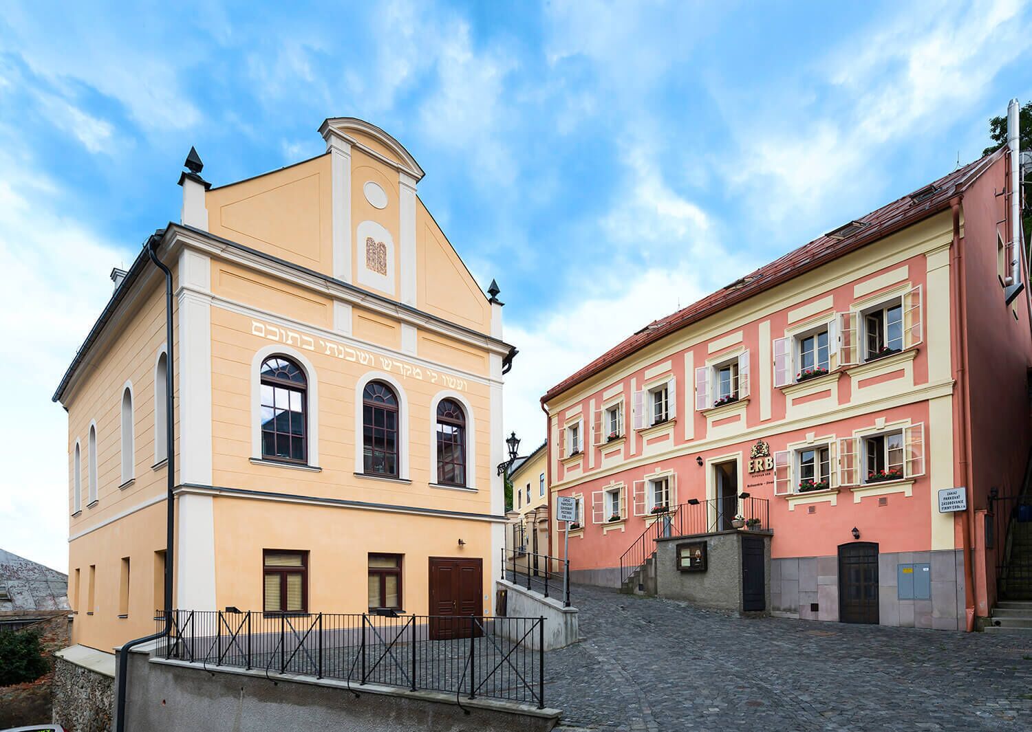 A historic building with a yellow facade and a red-roofed structure across the street.