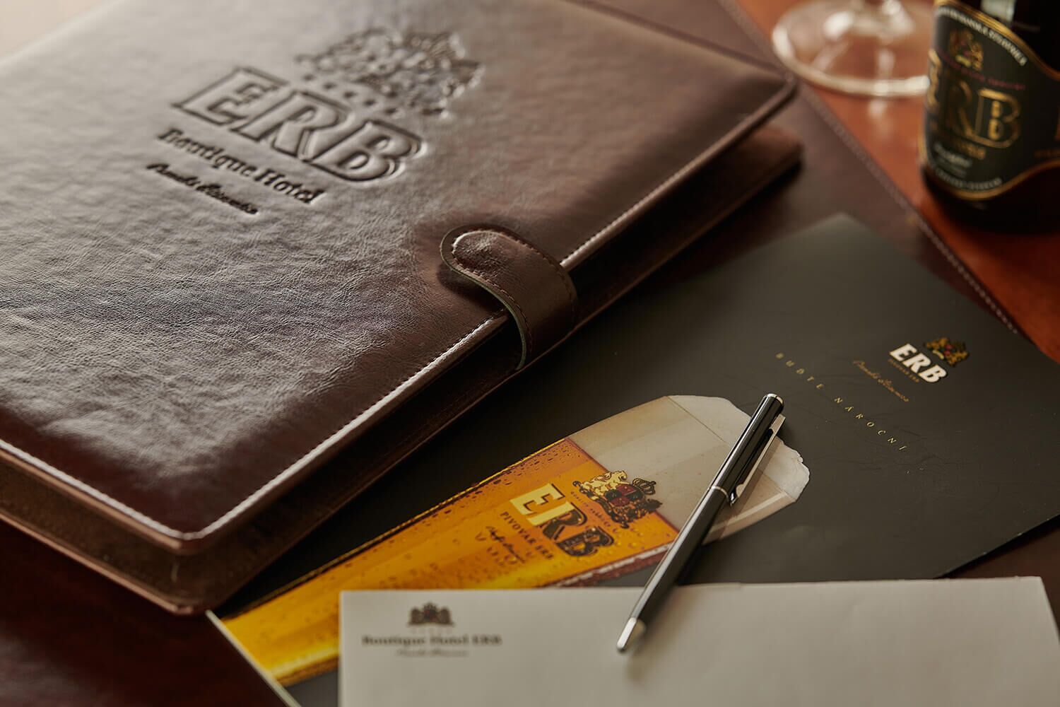A brown leather folder with embossed text, a pen, a business card, and a document on a wooden table.
