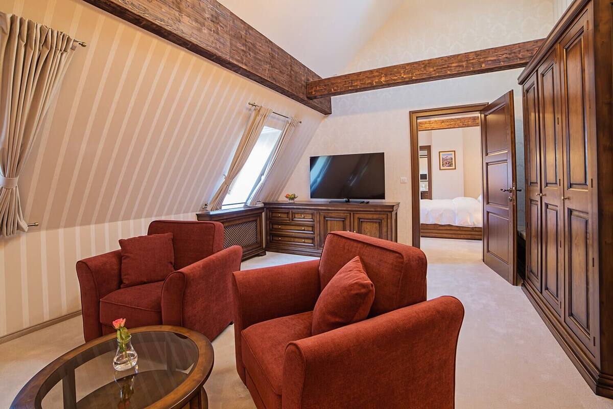 A hotel room with a red sofa set, a TV, a wooden cabinet, and a bed with a white duvet.