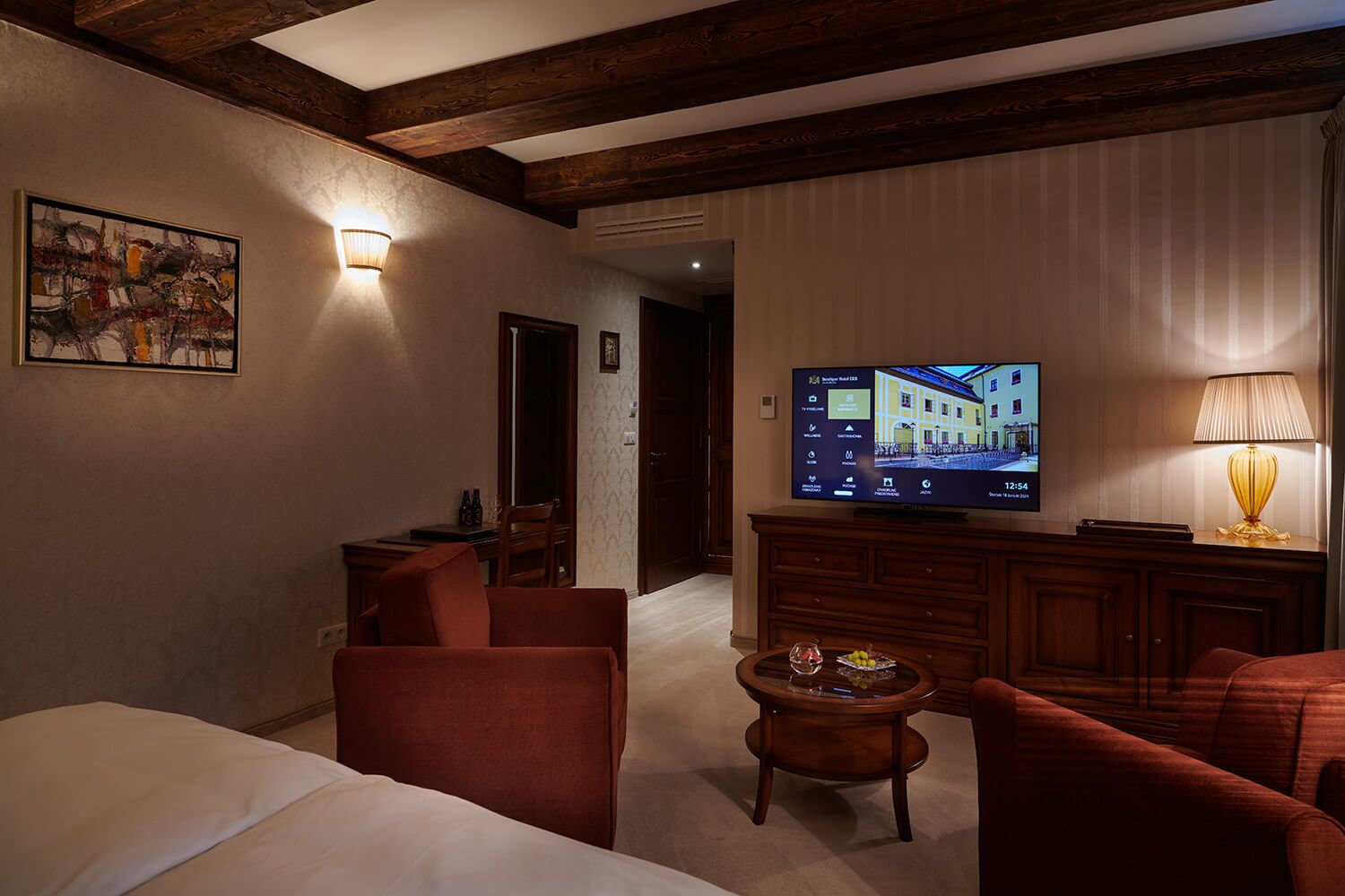 A hotel room with a bed, a TV, a desk, a chair, a lamp, and a painting on the wall.