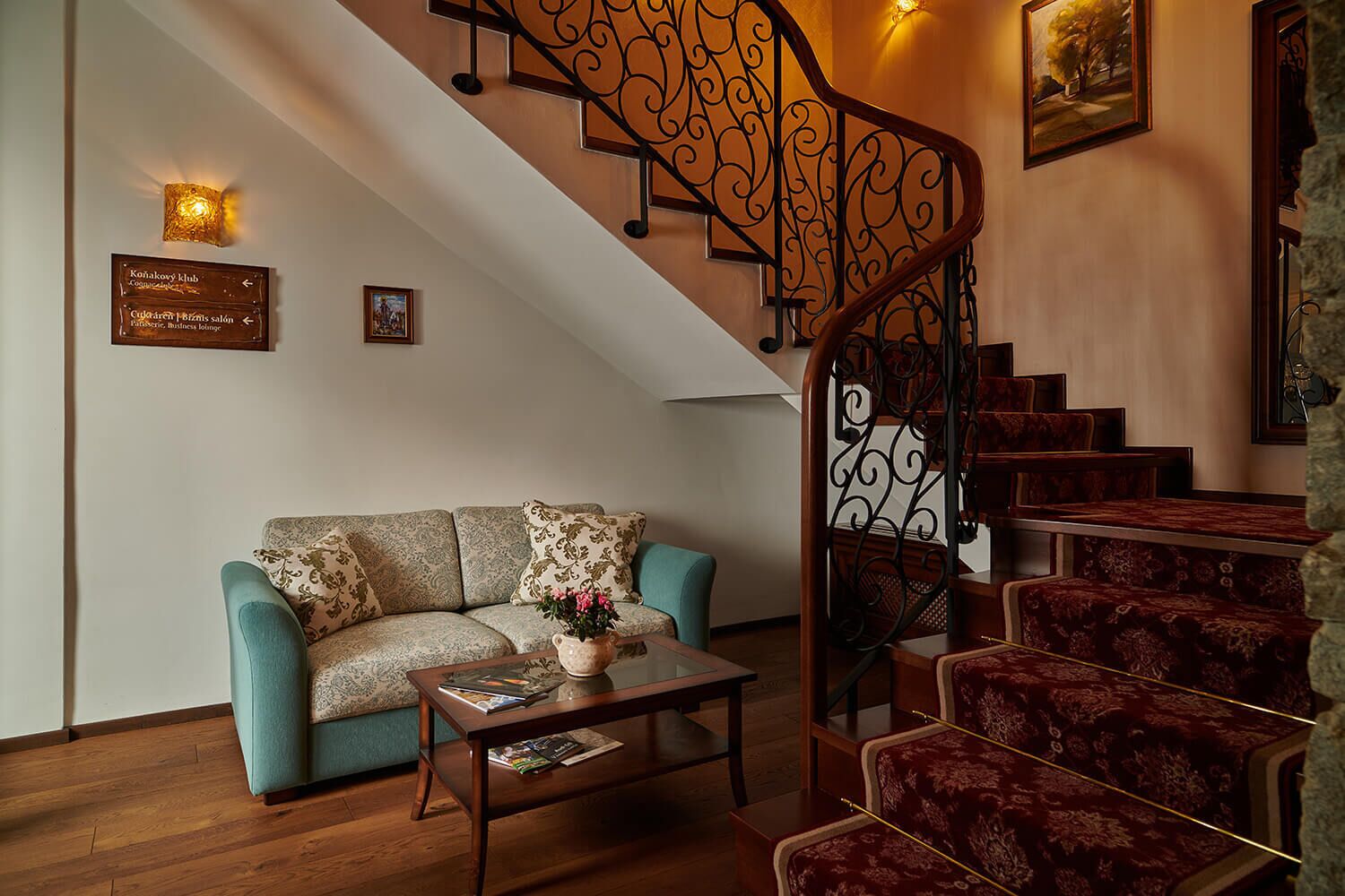 A staircase with ornate metal railings, a blue sofa with patterned cushions, and a wooden coffee table with magazines.