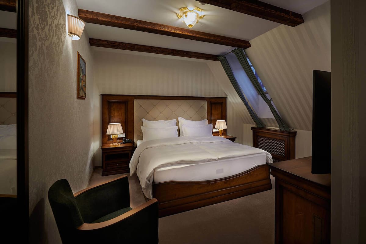 A hotel room with a large bed, two bedside tables with lamps, a chair, and a television.