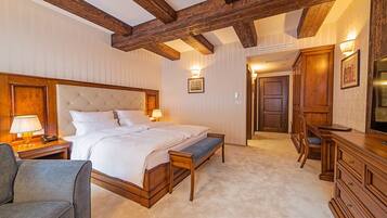 A hotel room with a large bed, bedside tables, a desk, a chair, and wooden beams on the ceiling.