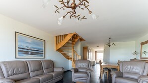 A living room with a sofa, armchairs, a wooden staircase, and a dining area.