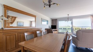 A dining area with a wooden table and chairs, a television, and a balcony with a view.
