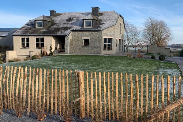A stone house with a sloped roof, a fenced yard, and a clear sky.