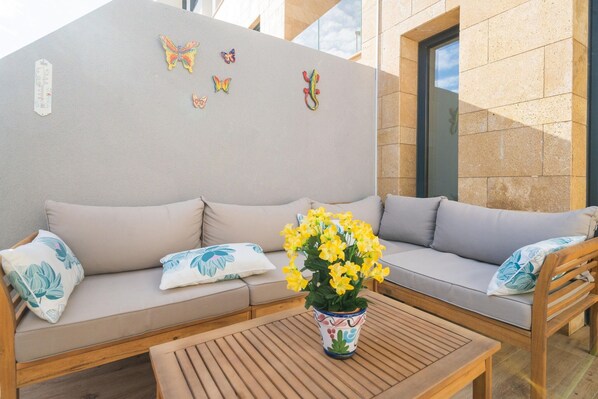 A modern outdoor seating area with a sofa and a wooden table, decorated with a potted plant and butterfly wall art.