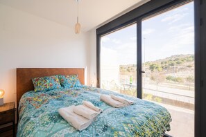 Ein Schlafzimmer mit einem großen Bett, einem Holzkopfstück und Blick auf einen Balkon mit Tisch und Stühlen.