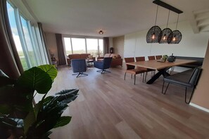 A spacious living area with a dining table, sofas, and chairs. There is a large window providing a view of the outdoors. - Family-Friendly Villa in Leons (Leons)