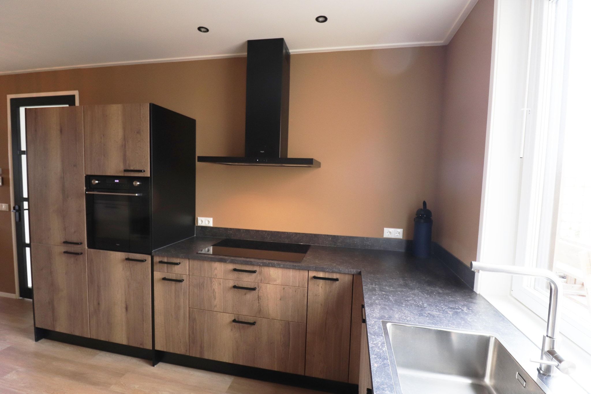 Una cocina moderna con armarios de madera, horno empotrado y un lavamanos de acero inoxidable.