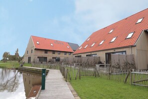 A modern building with a red-tiled roof and a wooden deck leading to a body of water. - Family-Friendly Villa in Leons (Leons)