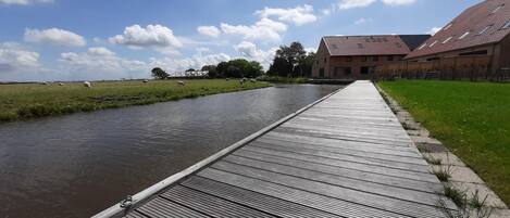 Un muelle de madera a orillas de un río tranquilo, que conduce a un edificio con techo inclinado.