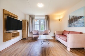 Una sala de estar con una televisión de pantalla plana, un mueble de madera, una mesa, dos sillas, un sofá y un cuadro en la pared.