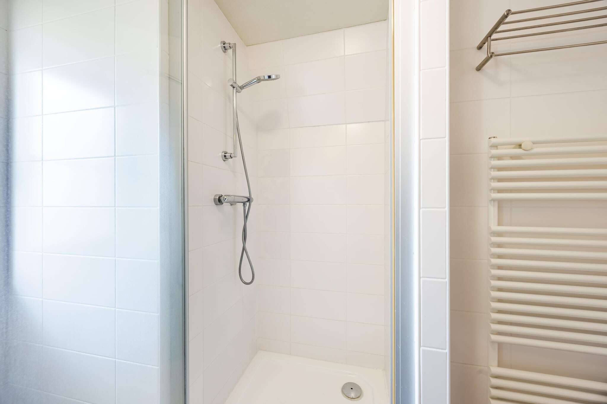 Eine Dusche mit Handbrause und Wandarmatur, eine weiße Duschkabine mit Fliesen und ein weißer Handtuchhalter.