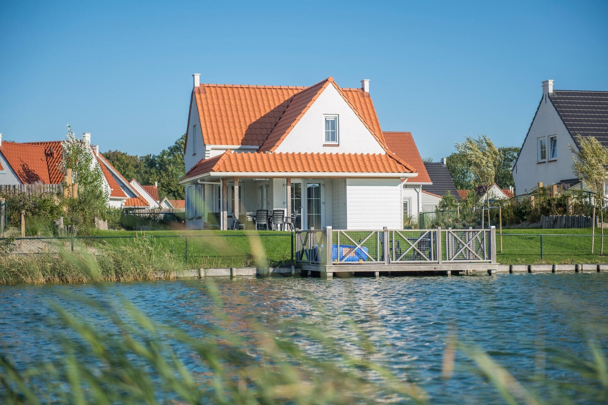 A house with a red-tiled roof, a dock, and a grassy area in front.