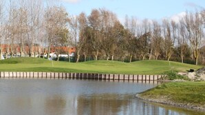 A golf course with a pond, trees, and a distant building. - Sleek Stay by the Sea (Middelkerke)