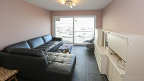 A living room with a black sofa, a small wooden table, and a white cabinet. - Sleek Stay by the Sea (Middelkerke)