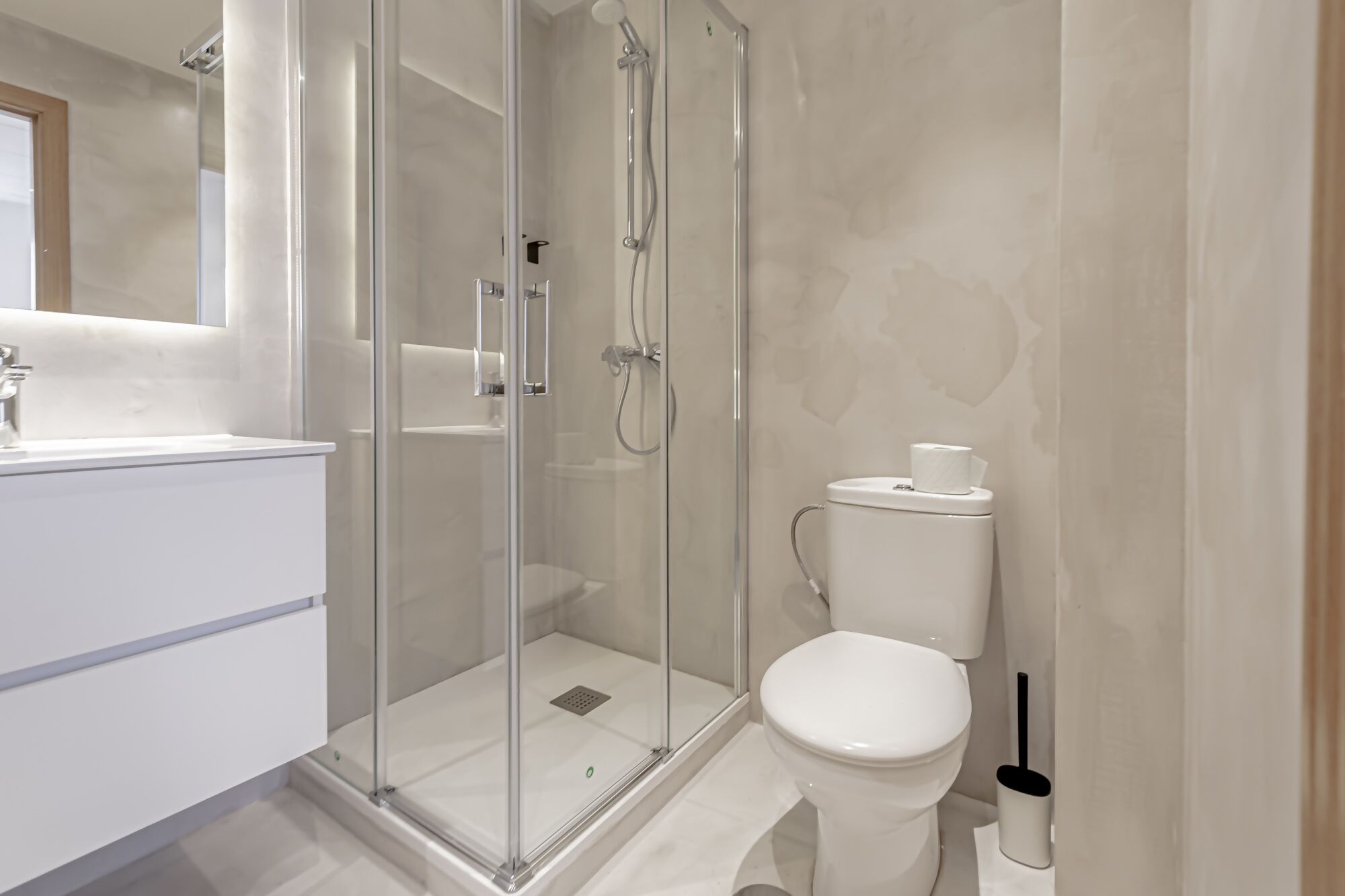 Een moderne badkamer met een douche met glazen wand, een wit toilet en een wastafel met spiegel.