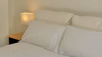 Un lit bien fait, avec du linge de lit blanc et des oreillers, une table de chevet avec une lampe et un mur sobre.
