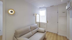 Una habitación con sofá, lámpara de pie, puerta y unidad de aire acondicionado.