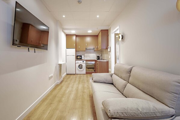 A compact living space with a sofa, a washing machine, a microwave, and a TV mounted on the wall.