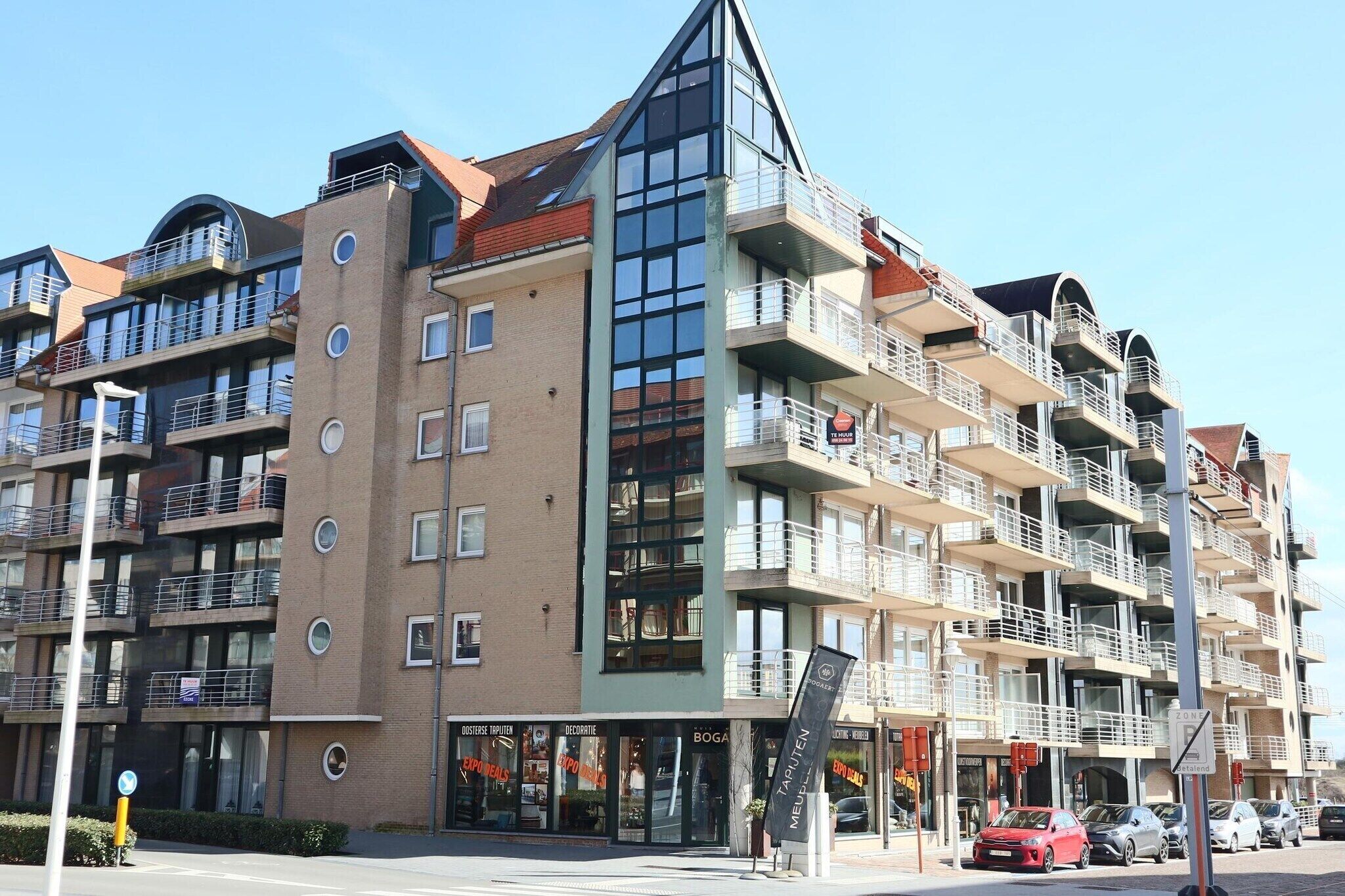 A multi-story hotel with balconies, a glass facade, and storefronts on the ground floor.