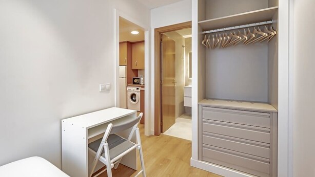 Una habitación compacta con kitchenette, armario empotrado y escritorio plegable.
