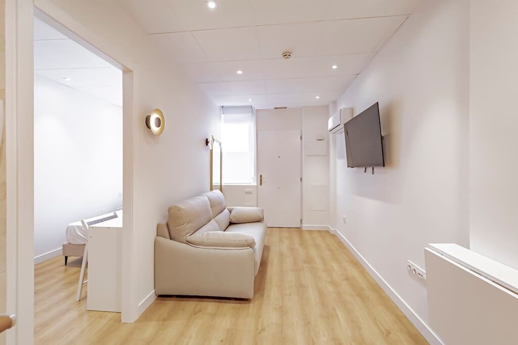 A modern living room with a beige sofa, a flat-screen TV mounted on the wall, and a wooden floor.