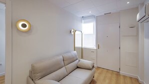 Una sala moderna con un sofá color crema, una lámpara de pie y una puerta que da a otra habitación.