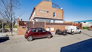 Un coche rojo estacionado frente a un edificio de fachada de ladrillo y una valla metálica.