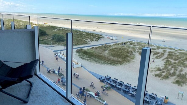 A beach view from a balcony with a chair, tables, and a grassy area. - Studio in Nieuwpoort near the Beach (Nieuwpoort)