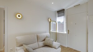 A modern living room with a beige sofa, a small round table, and a window with blinds. - New Apartment Madrid Feria 103 (Madrid)