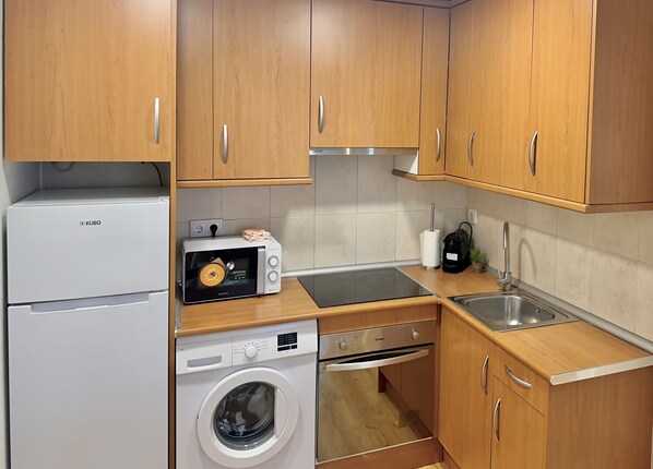 A compact kitchen with wooden cabinets, a microwave, a washing machine, and a sink. - New Apartment Madrid Feria 105 (Madrid)
