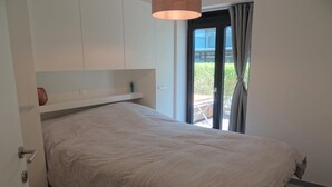 Een slaapkamer met een bed, een raam met gordijnen en een deur.