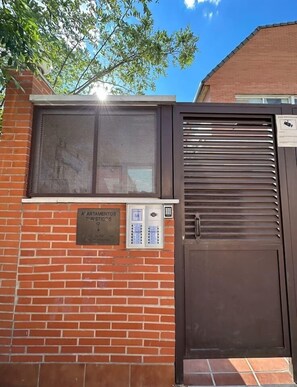 Un mur de briques avec un portail en métal, une fenêtre munie d’un moustiquaire et une serrure à clavier.