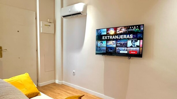 A hotel room with a bed, a TV displaying a channel called "EXTRANGERAS," and a wall-mounted air conditioner.