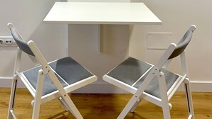 Una mesita pequeña y blanca plegable con dos sillas grises con acolchado.