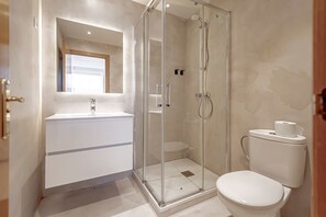 A modern bathroom with a glass-enclosed shower, a white sink, and a toilet.